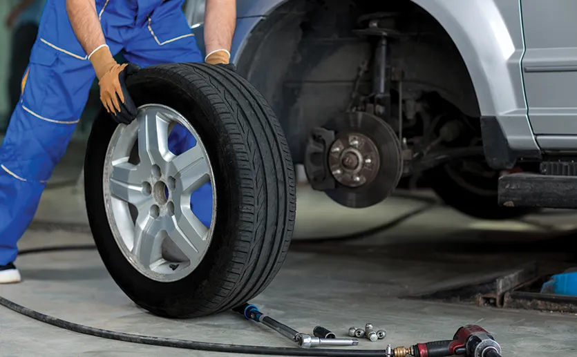 Mechanik nasazuje kolo s novou pneumatikou na vůz v servisu